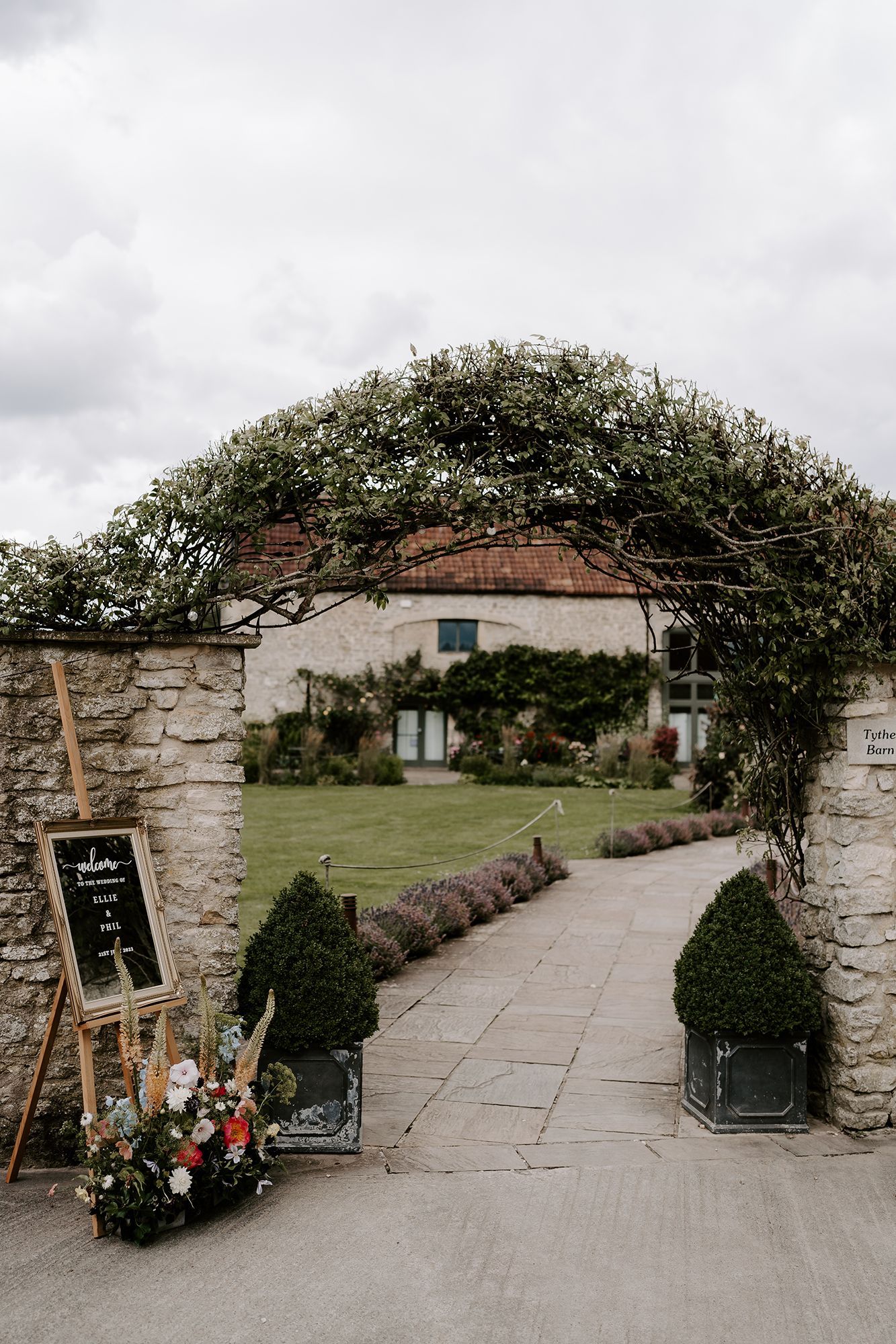 A stone archway leading to a house with flowers in front of it.