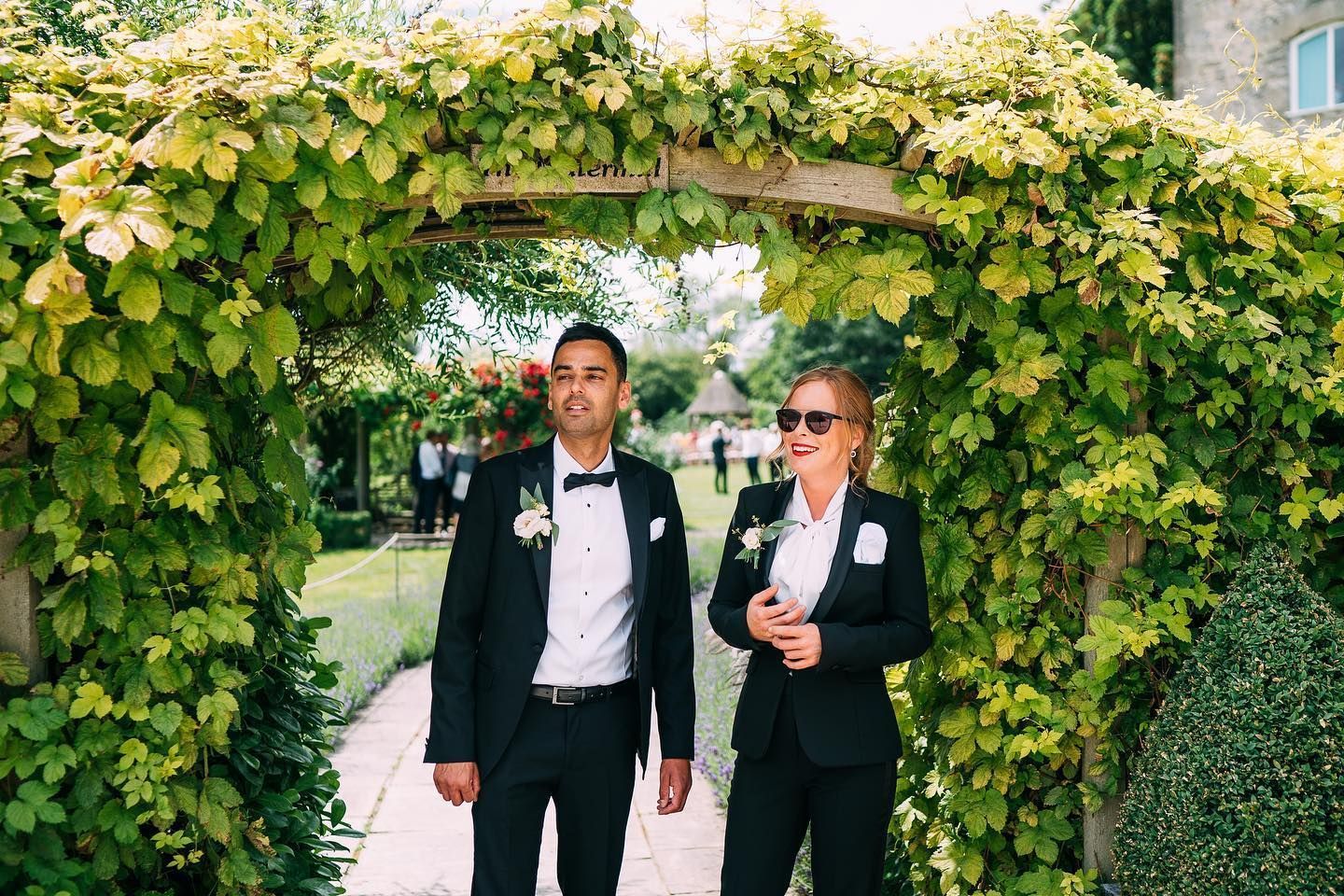 A man and a woman in suits are standing under an archway.