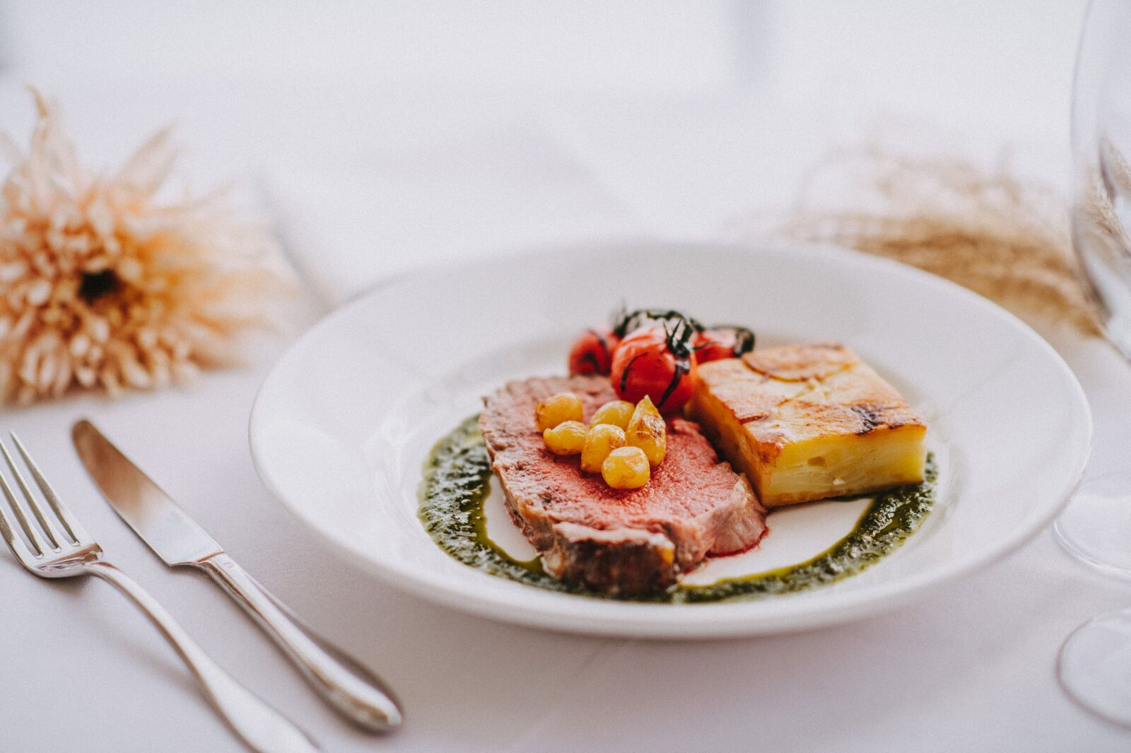 A white plate topped with a piece of meat and potatoes on a table.