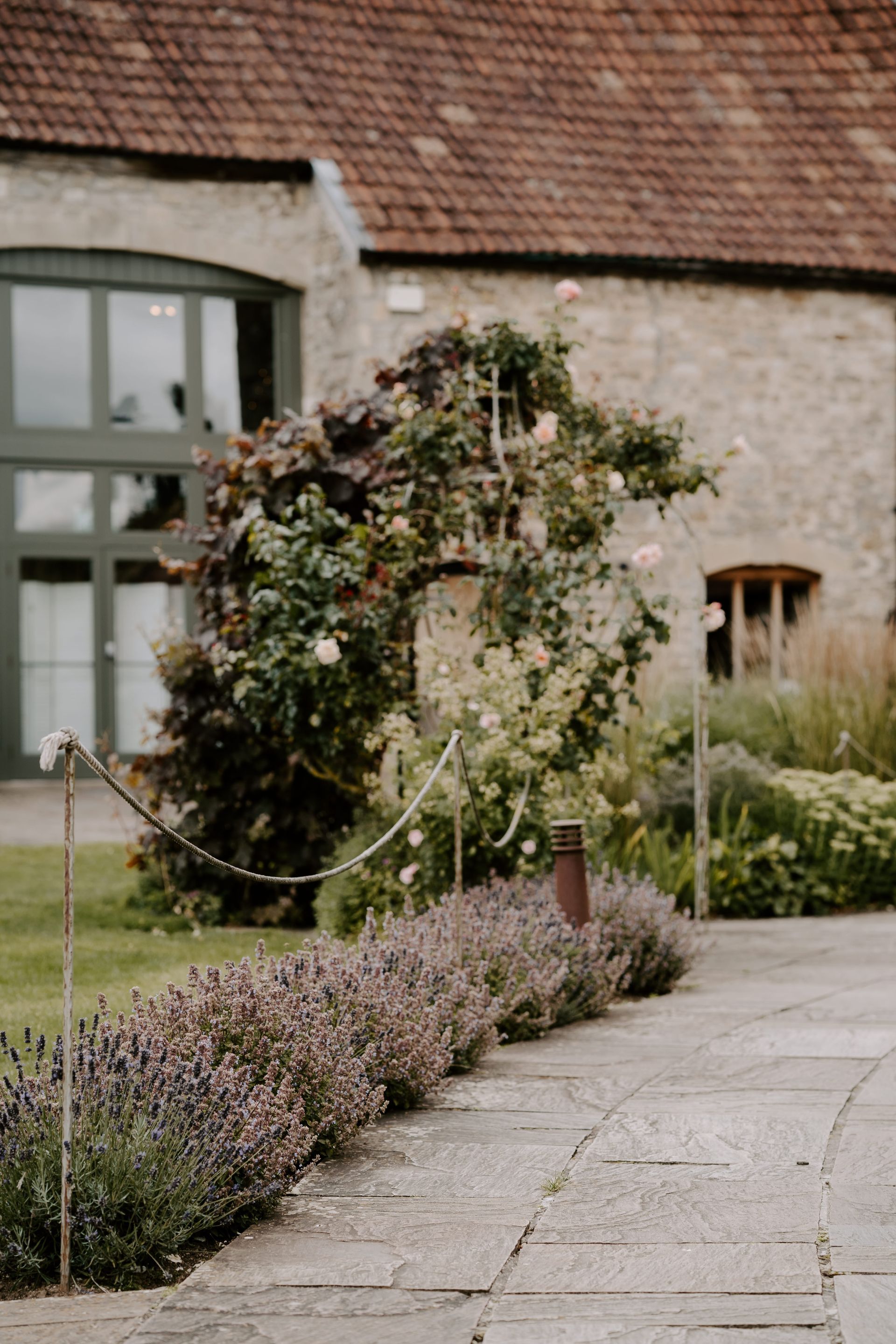 A stone walkway leading to a building surrounded by flowers and trees.