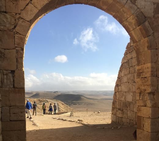 Stone archway framing a desert landscape with people observing the view under a blue sky.