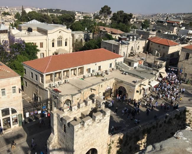 Overhead view of Jerusalem buildings with a crowd, possibly a celebration, gathered near a stone tower.