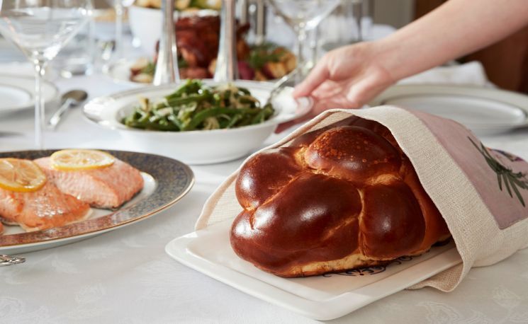 challah bread in the foreground of a table set for shabbat dinner