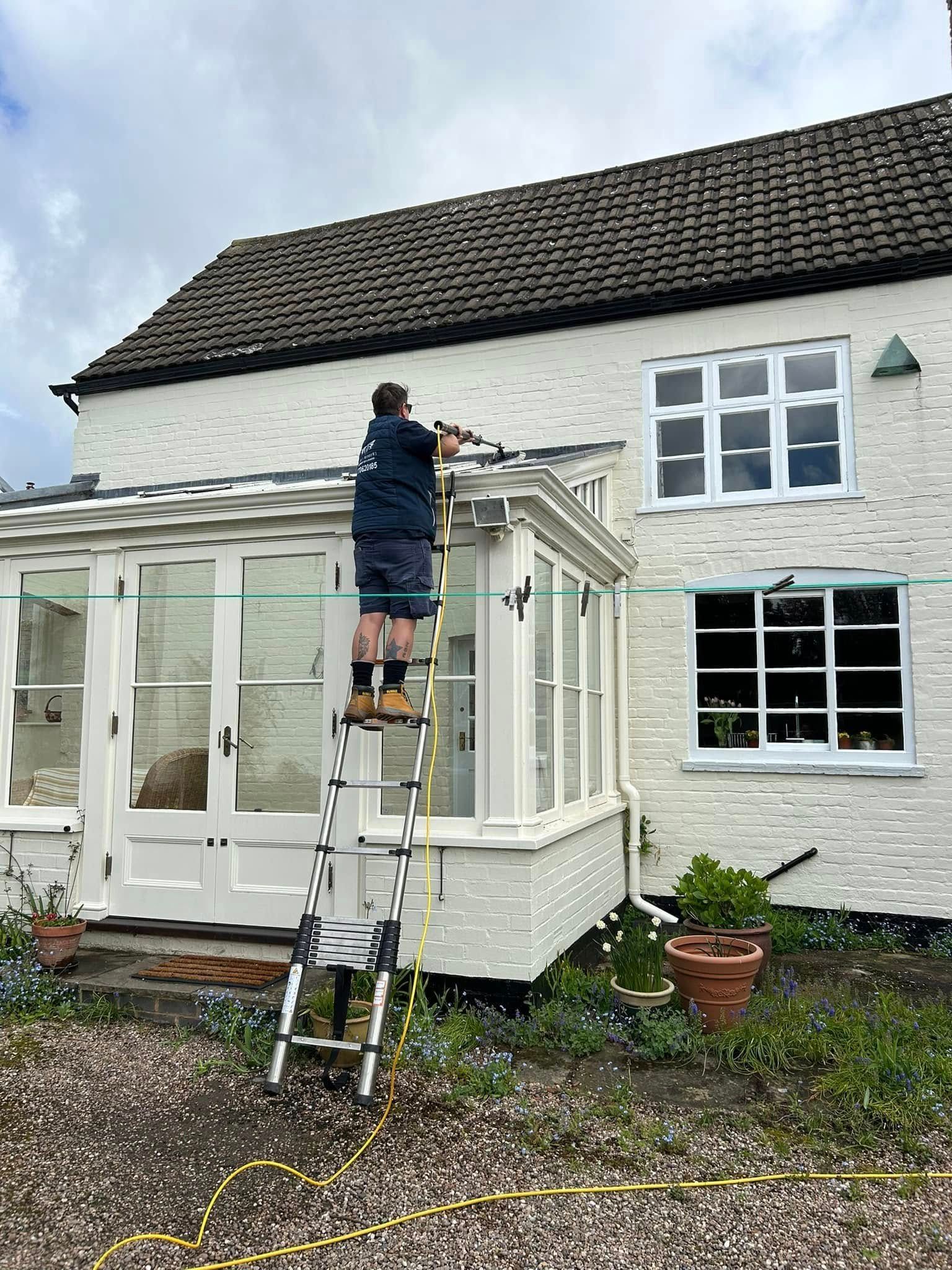 Person on a ladder repairing the roof above a white house porch