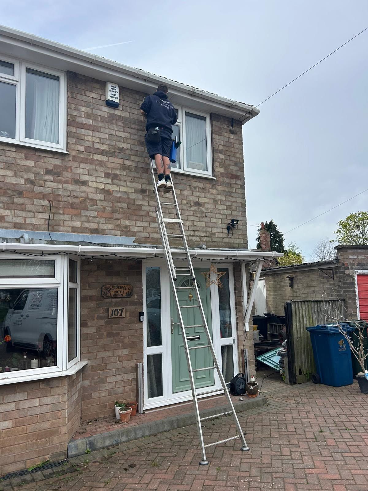 Person on a ladder cleaning a second-floor window of a brick house