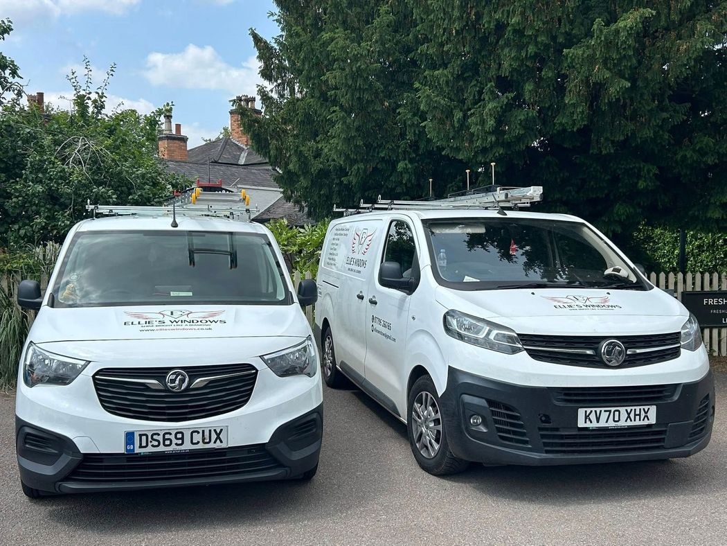 Two white service vans parked side by side on a residential street under trees.