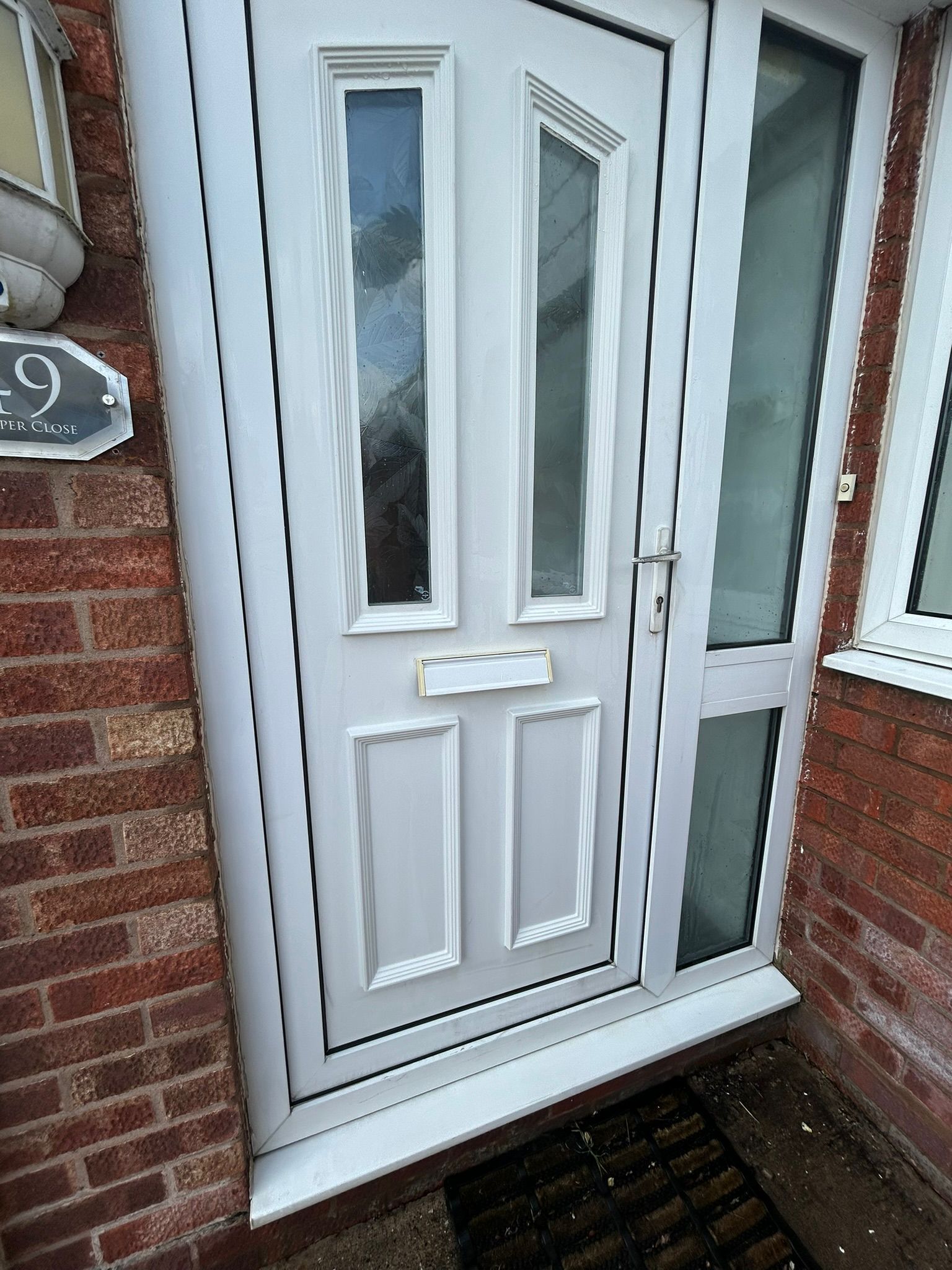 White front door with narrow glass panels and side window beside a red brick wall.