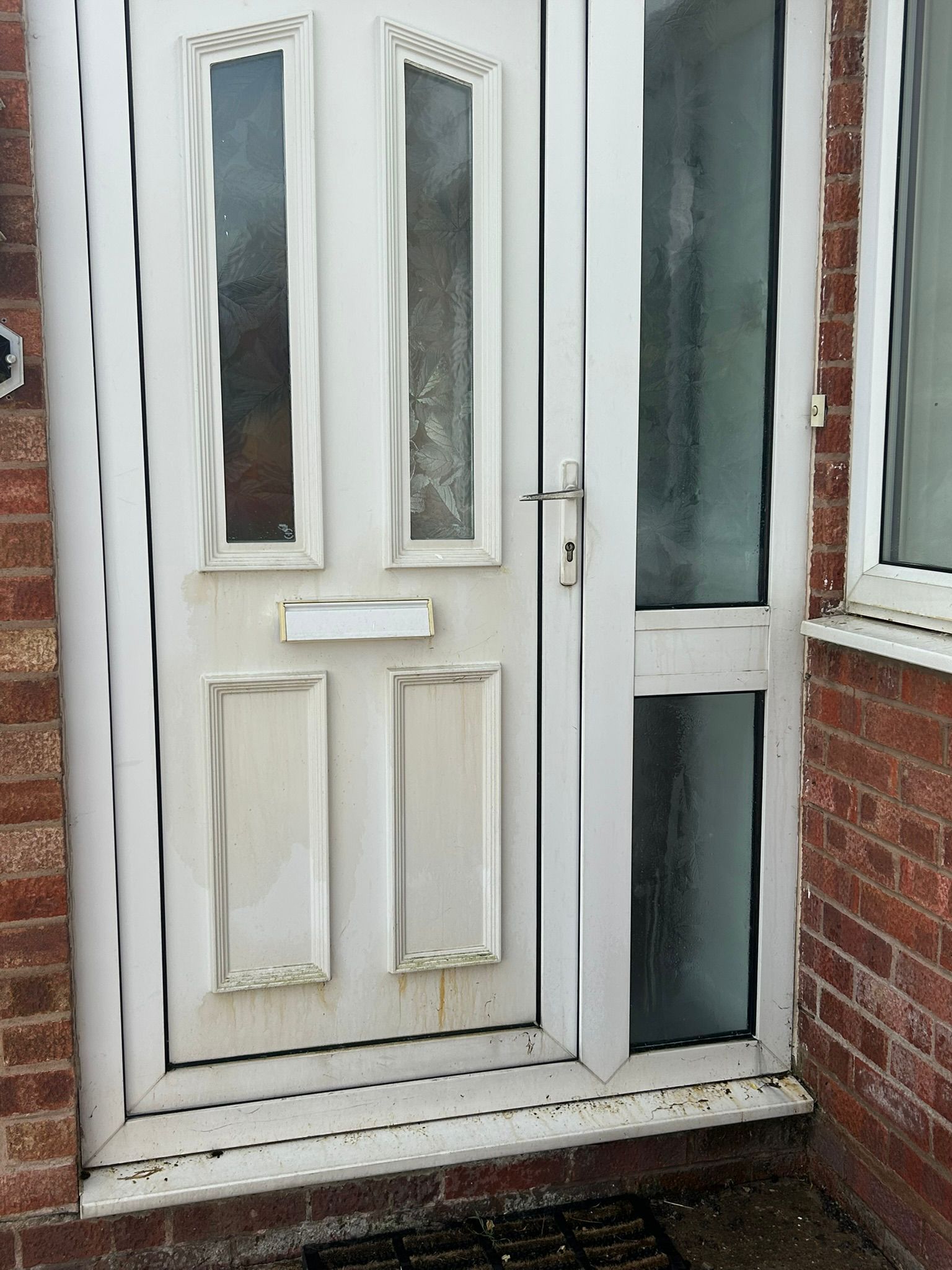 White front door with frosted glass panels beside a narrow side window in a brick entryway