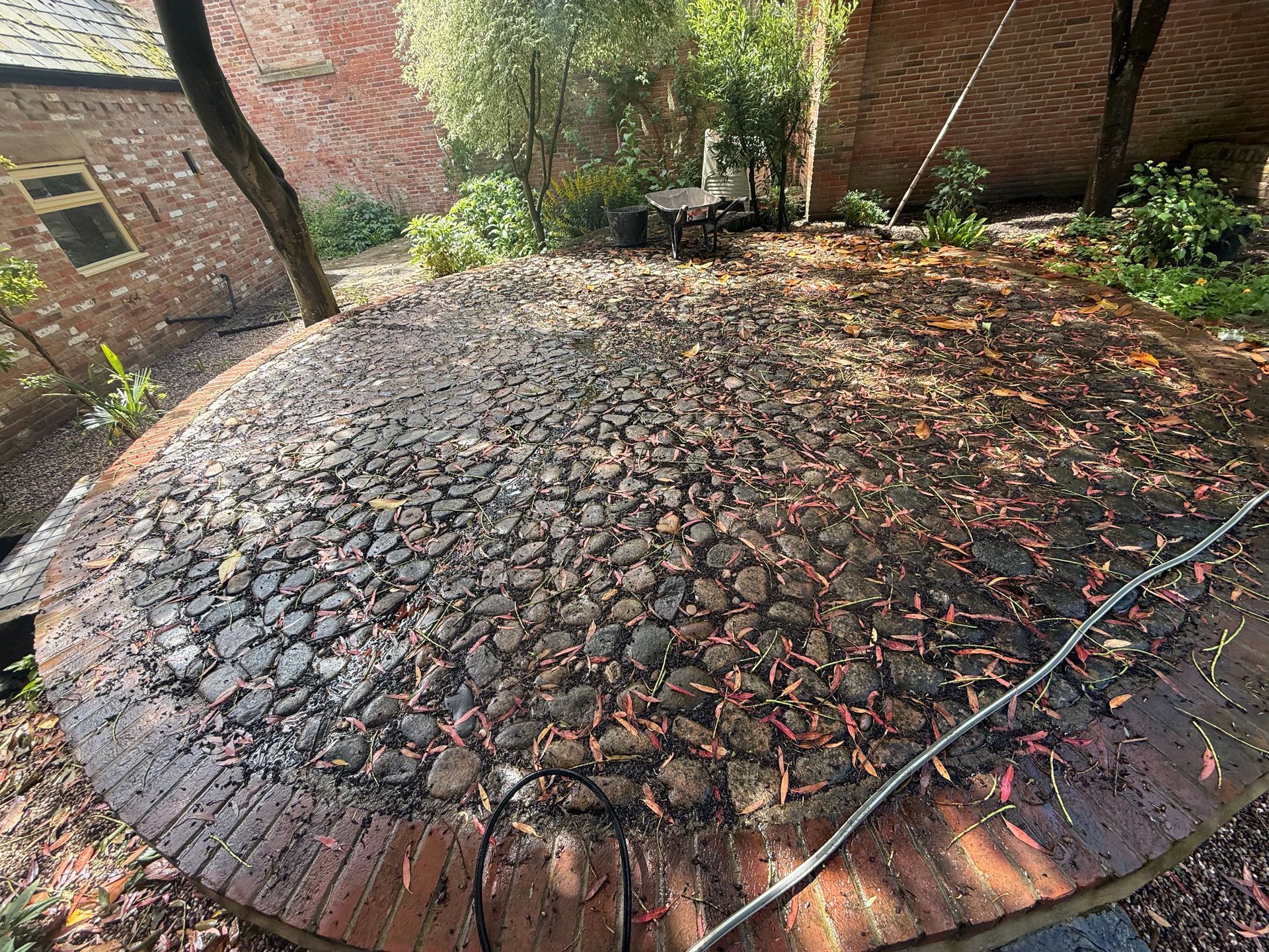 Circular brick fire pit covered with leaves in a small backyard garden