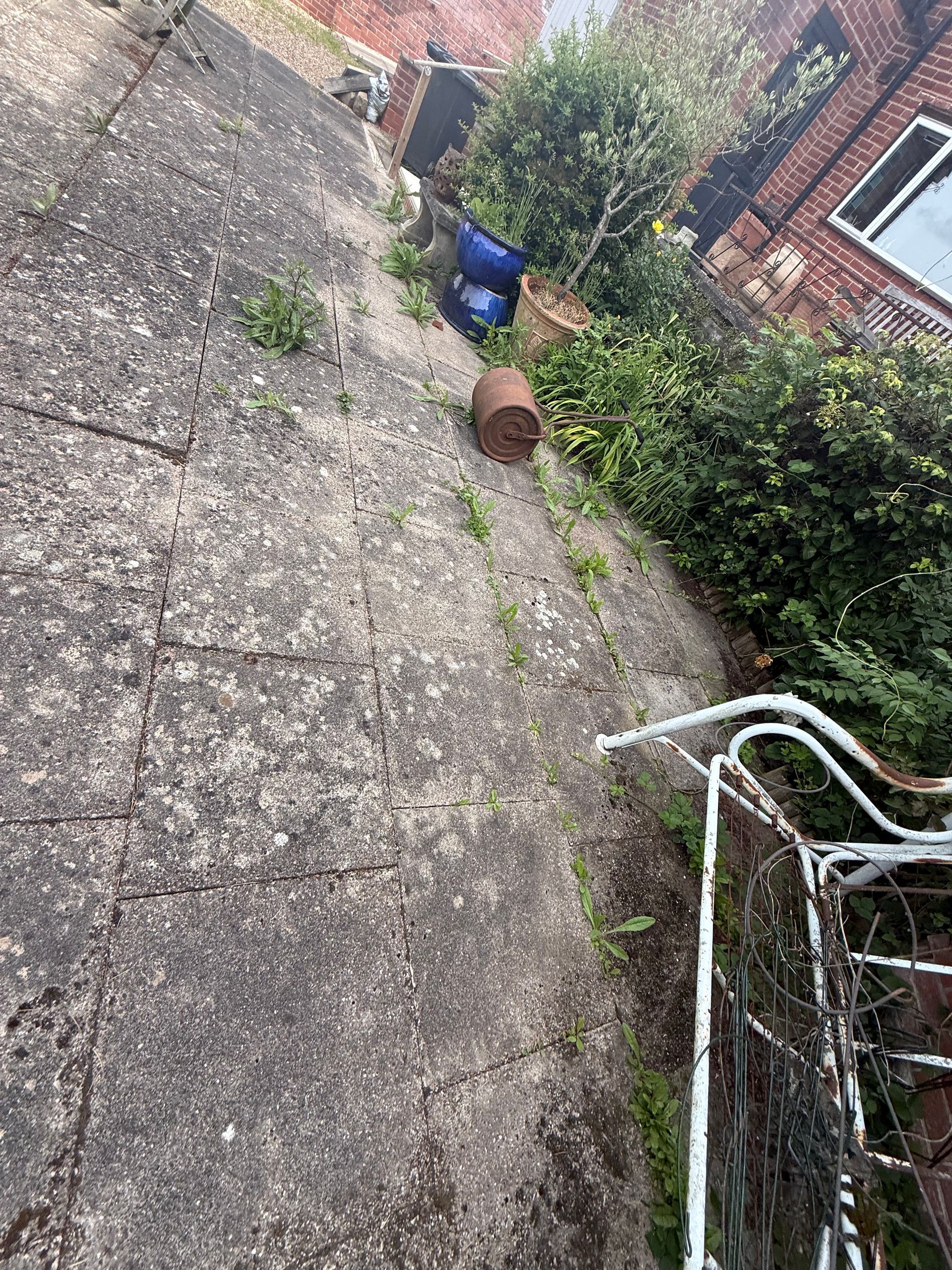 Tilted view of a gravel patio with a blue bin, brick wall, bushes, and a white metal chair in the foreground