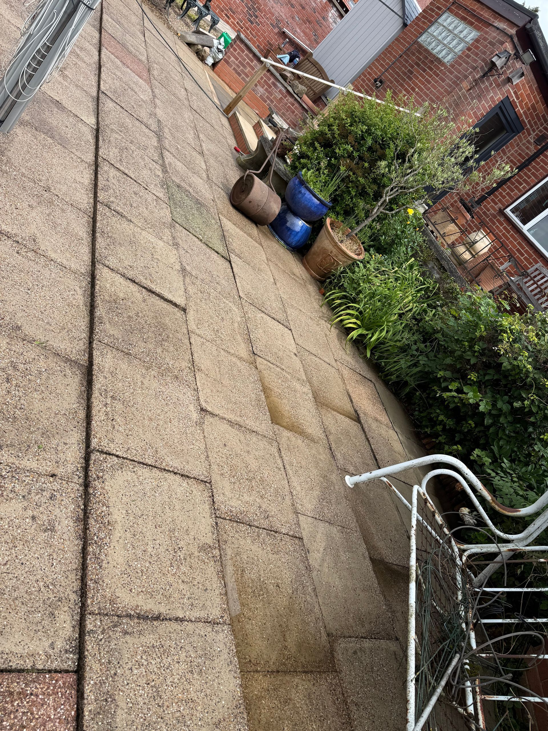 Tilted view of a rooftop patio with gravel paving, potted plants, and a metal chair beside brick houses