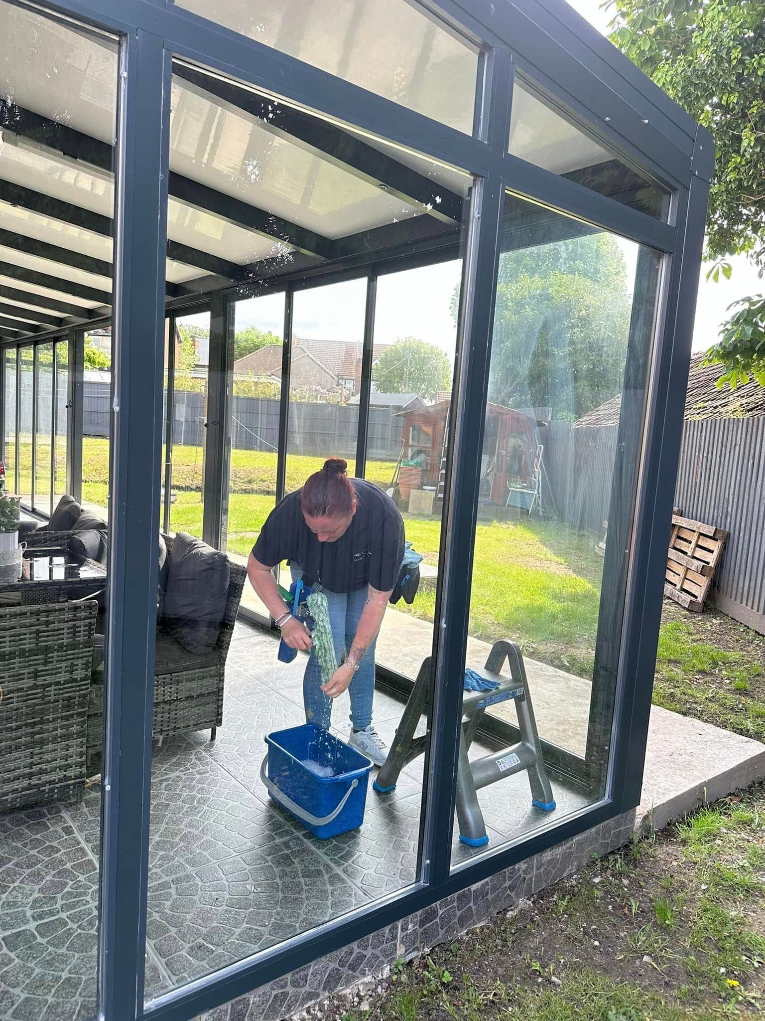 Person mopping the floor inside a glass patio enclosure with a blue bucket.