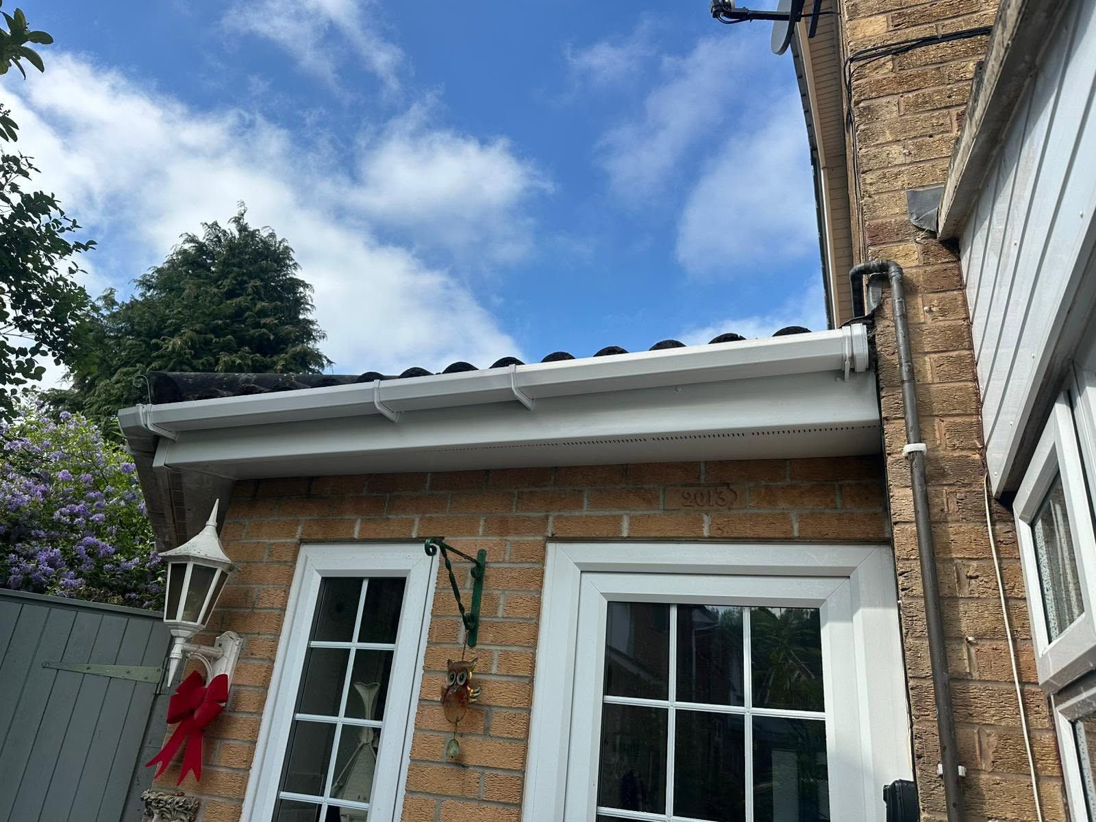 Brick house exterior with white-framed windows, roof eaves, and a red holiday bow under a blue sky