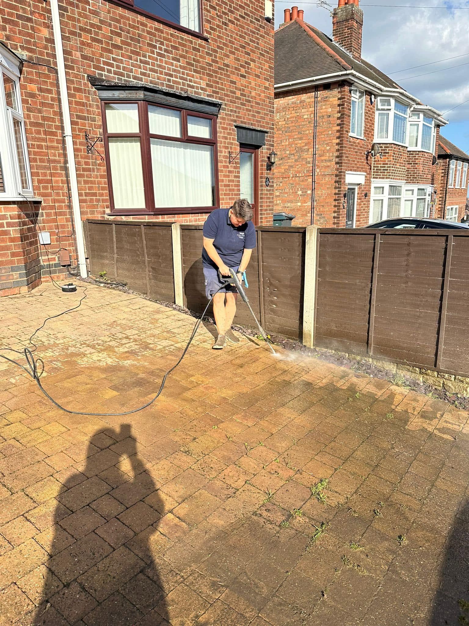 Zoe using a pressure washer to clean a brick patio in a sunny backyard