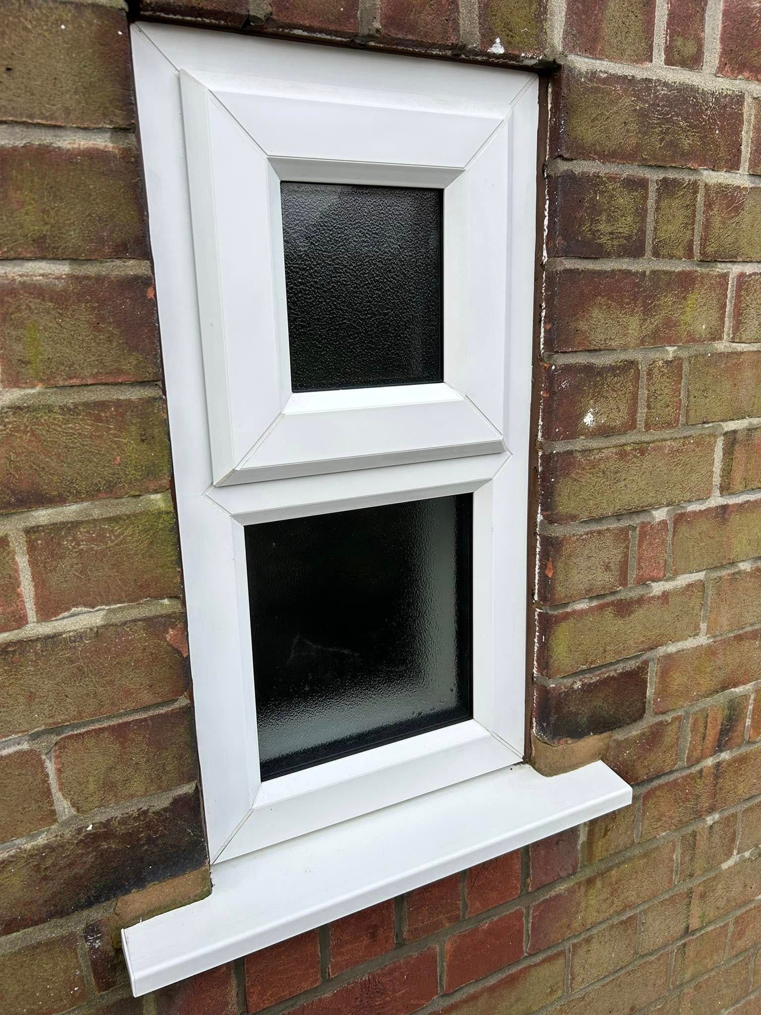 Two white-framed windows on a brick wall, with frosted glass and a small sill underneath.