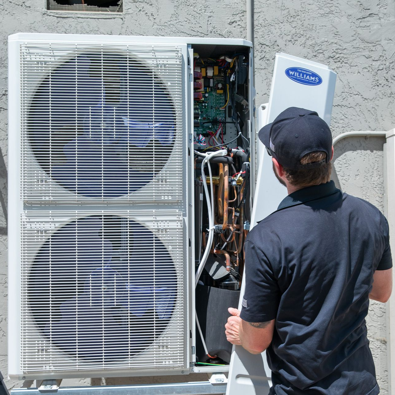 Williams Mechanical Co technician removing the side panel of a heat pump outdoors