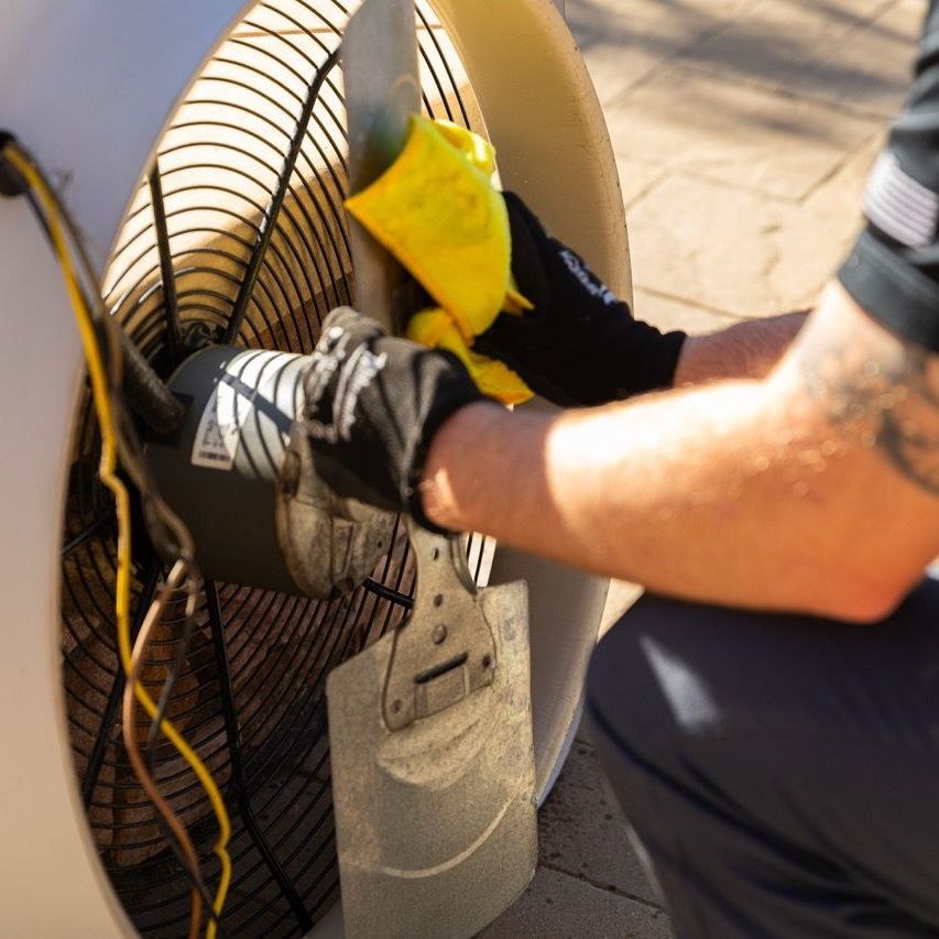 Person cleaning an air conditioner fan with a yellow cloth, outdoors.