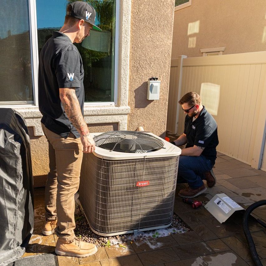 Williams Mechanical Co technicians installing an air conditioner outside a home
