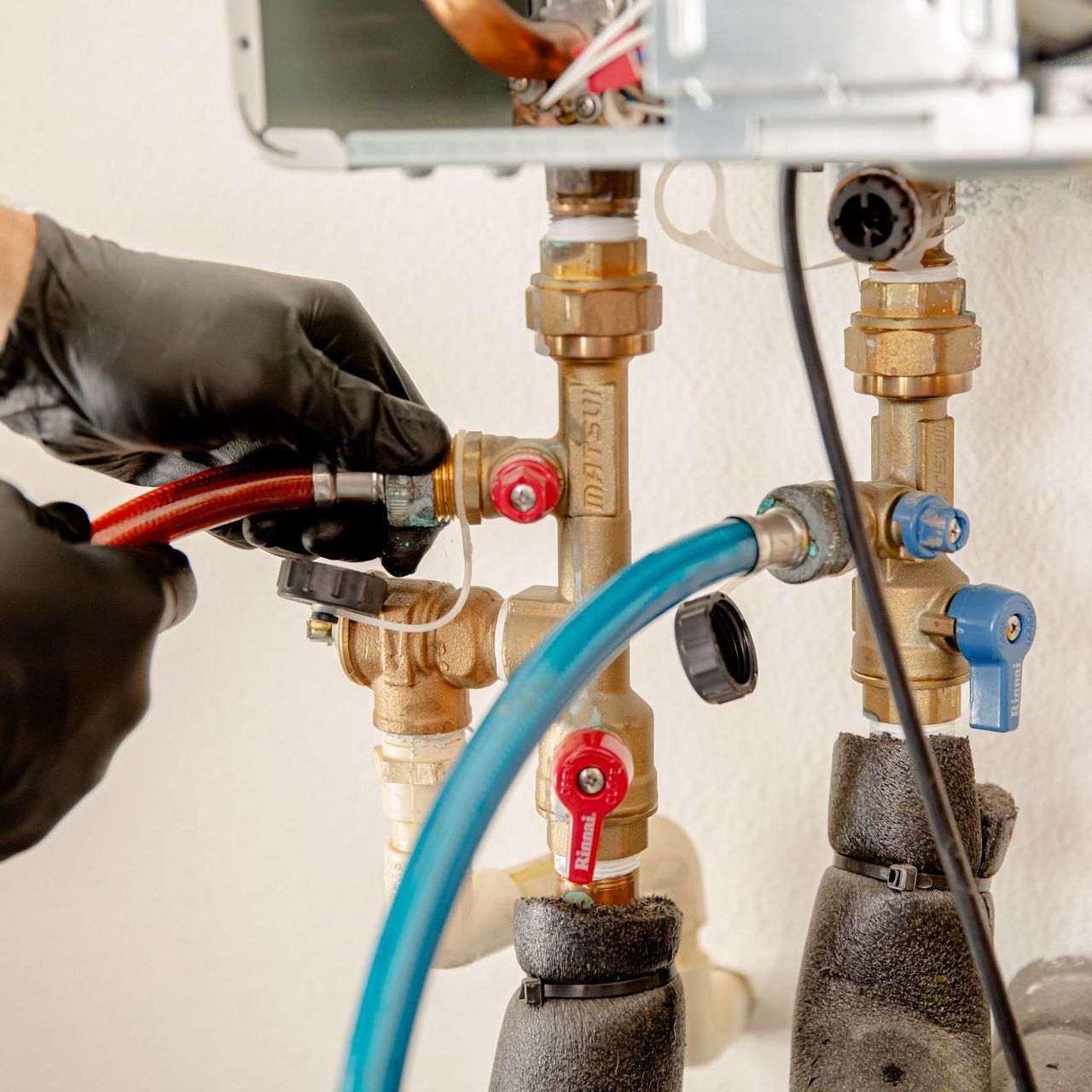 Williams Mechanical Co technician connecting hoses to a tankless Rinnai water heater.