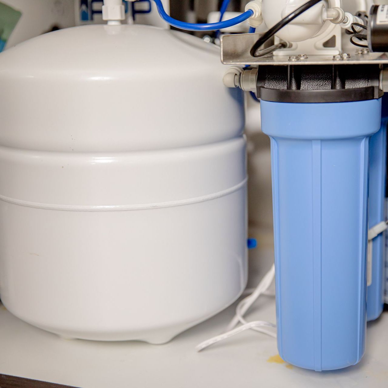 A white water storage tank next to a vertical blue filter housing unit under a sink.