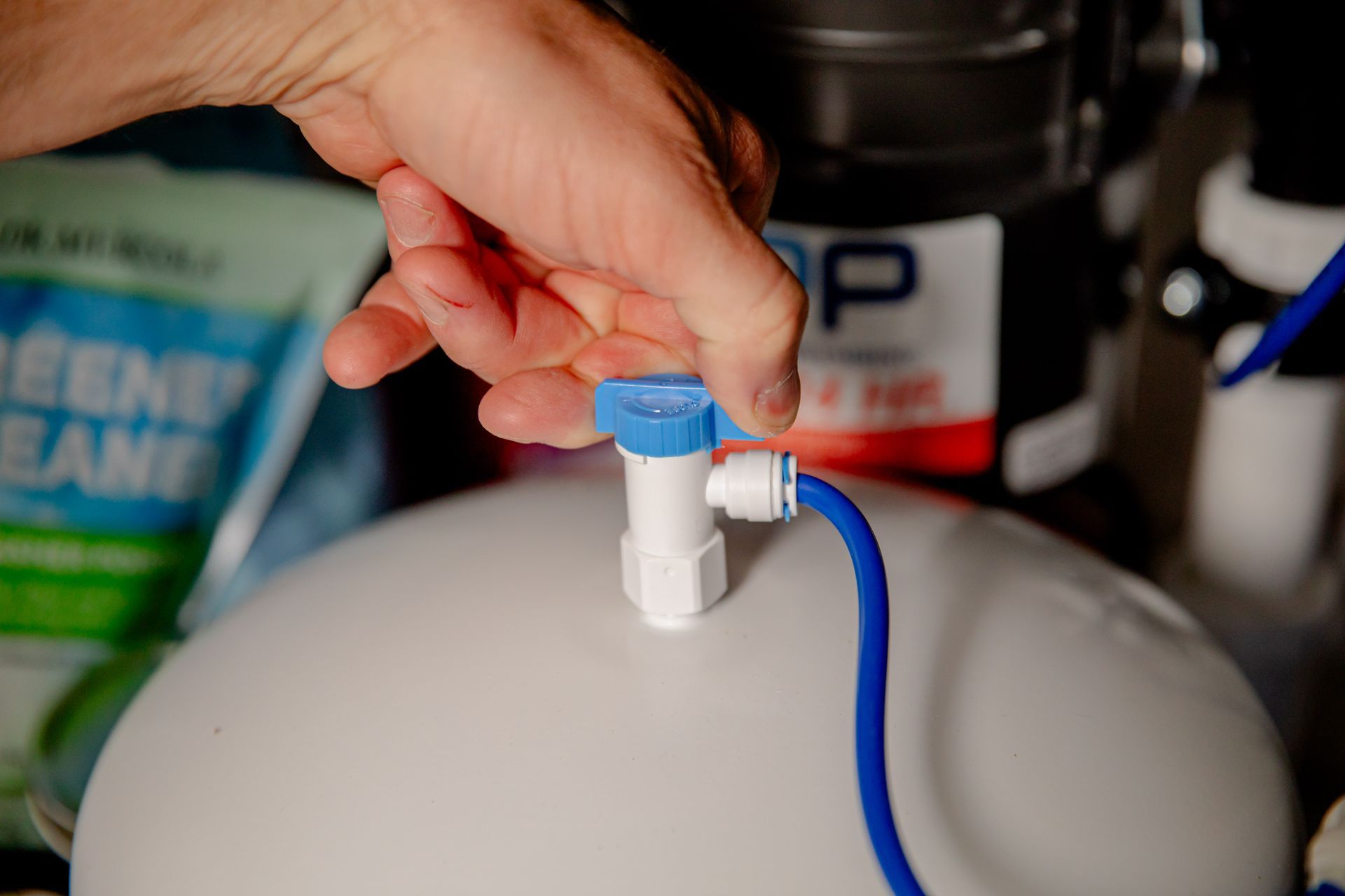 A hand turning the blue valve on top of a white water filtration storage tank.