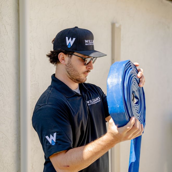 Williams Mechanical Co technician holding a water hose on a job site