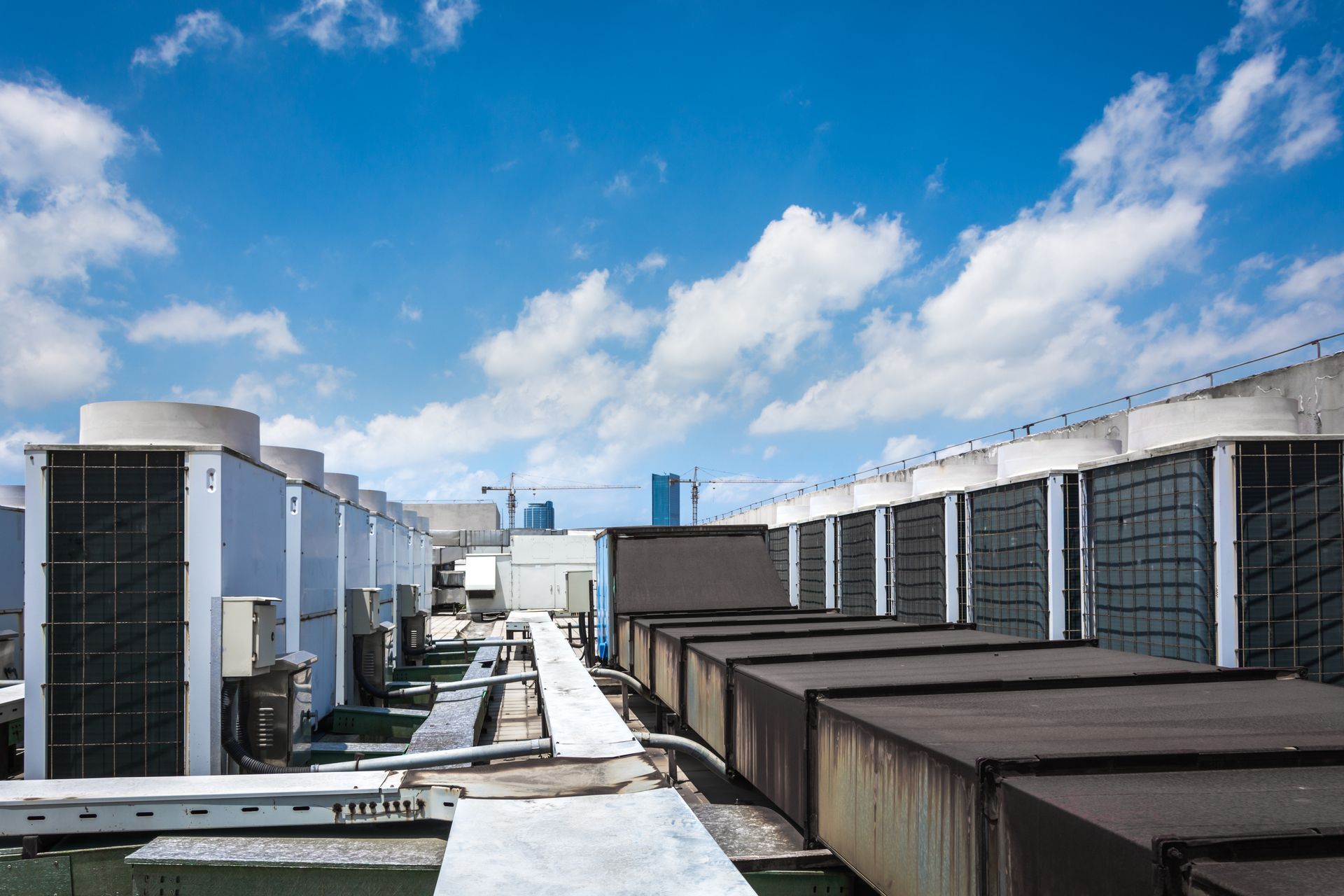 Rooftop with multiple air conditioning units and ductwork under a blue sky with clouds.