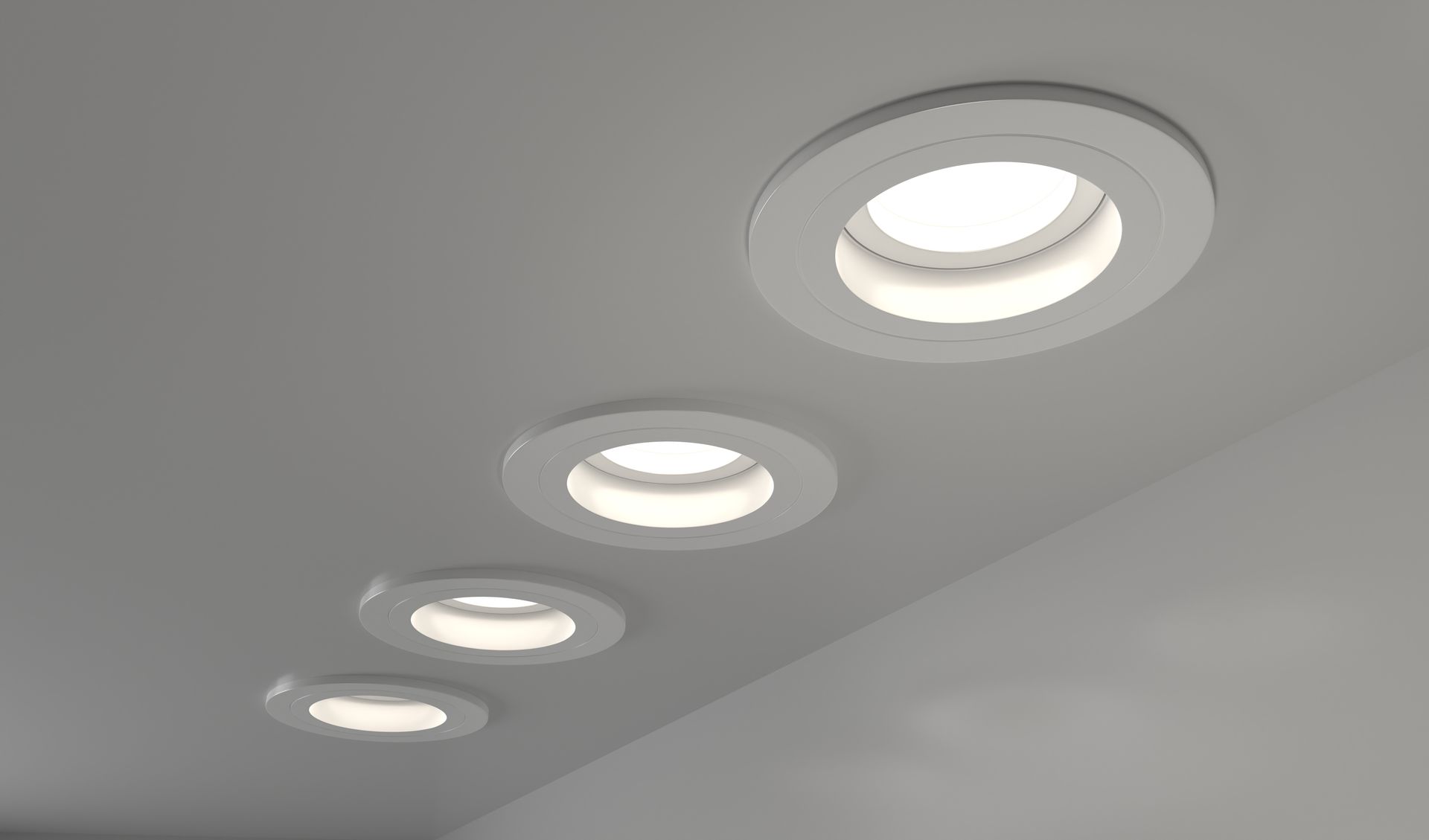 Four circular, recessed white lights are mounted in a diagonal row on a plain, light-gray ceiling.