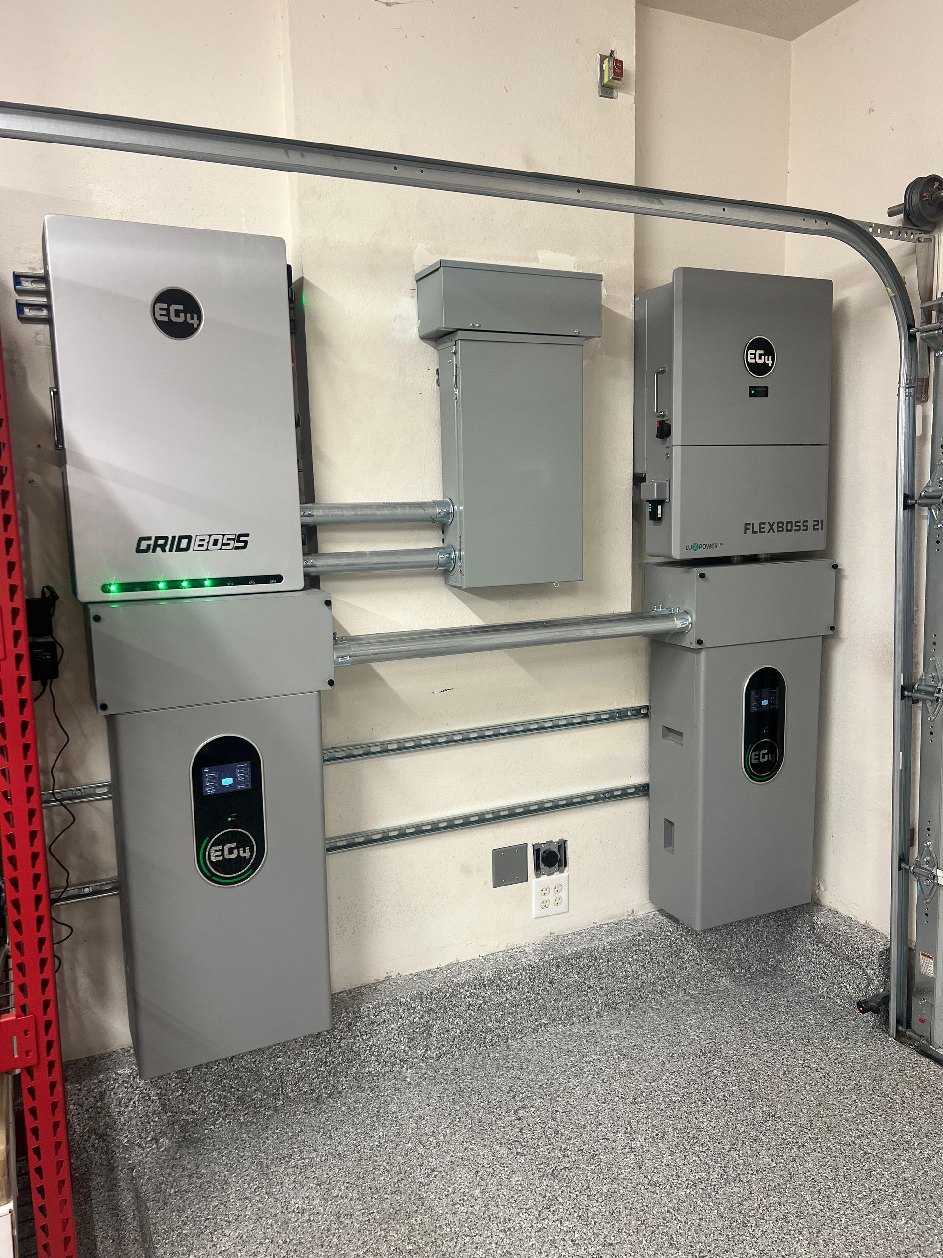 Two gray solar energy EG4 inverters with battery storage units mounted on a garage wall with conduit wiring.