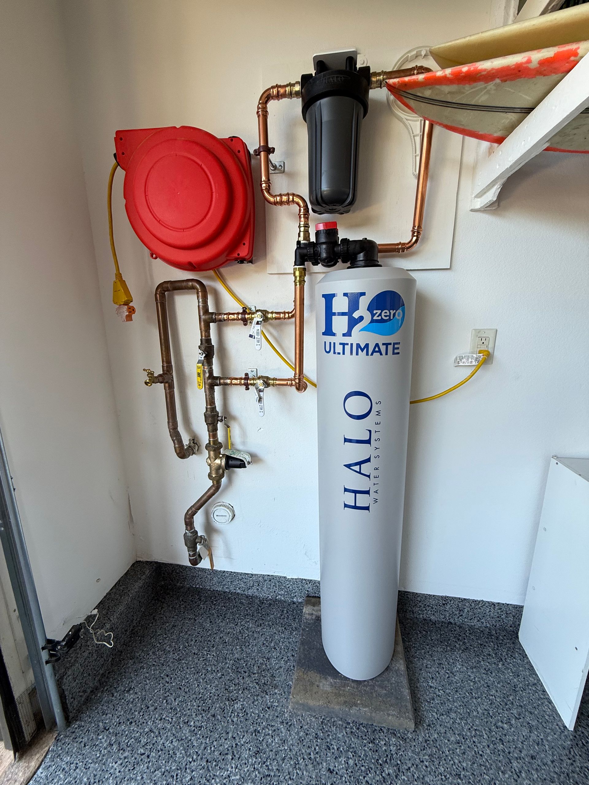 Halo Water filtration system with copper piping, a large cylindrical tank, and a red reel in a garage.