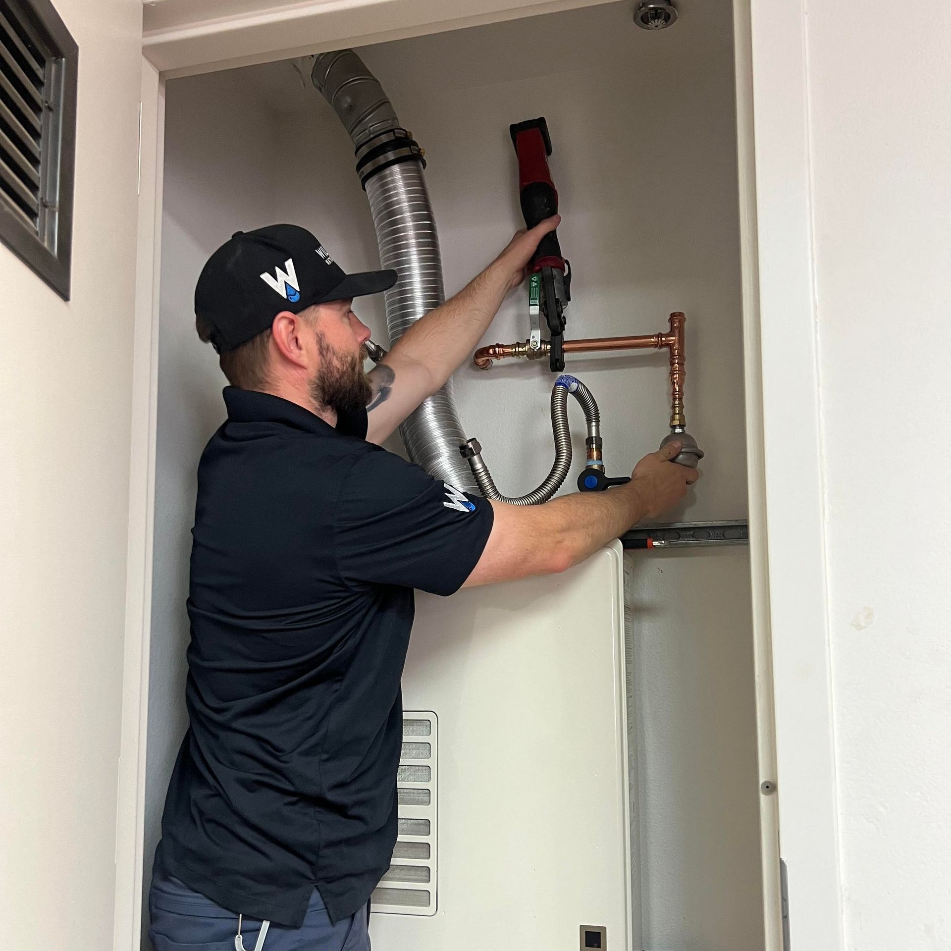 A technician in a black uniform works on a Nortiz tankless water heater inside a utility closet.