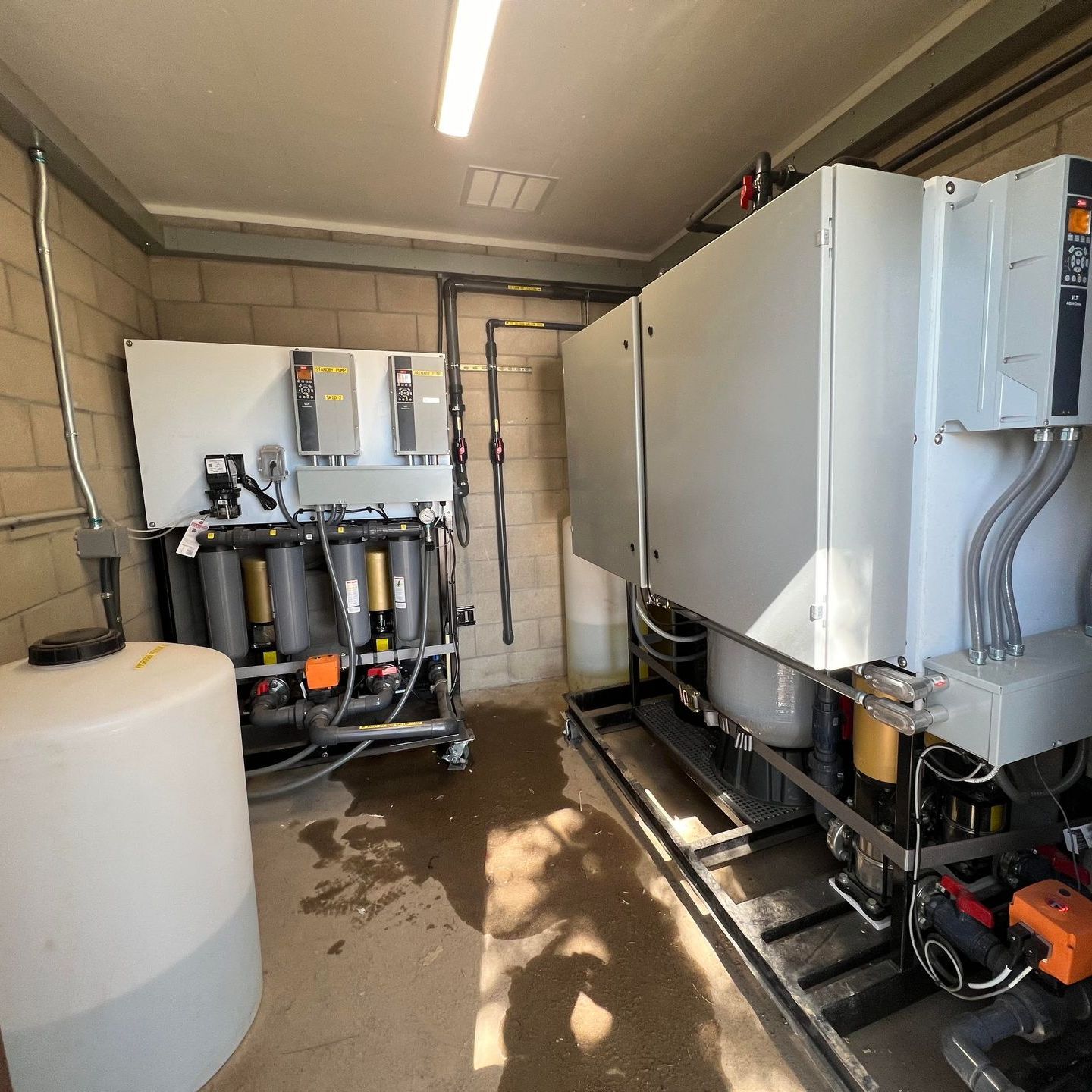Well water treatment system in a utility room with PLC, plumbing, and water filtration.