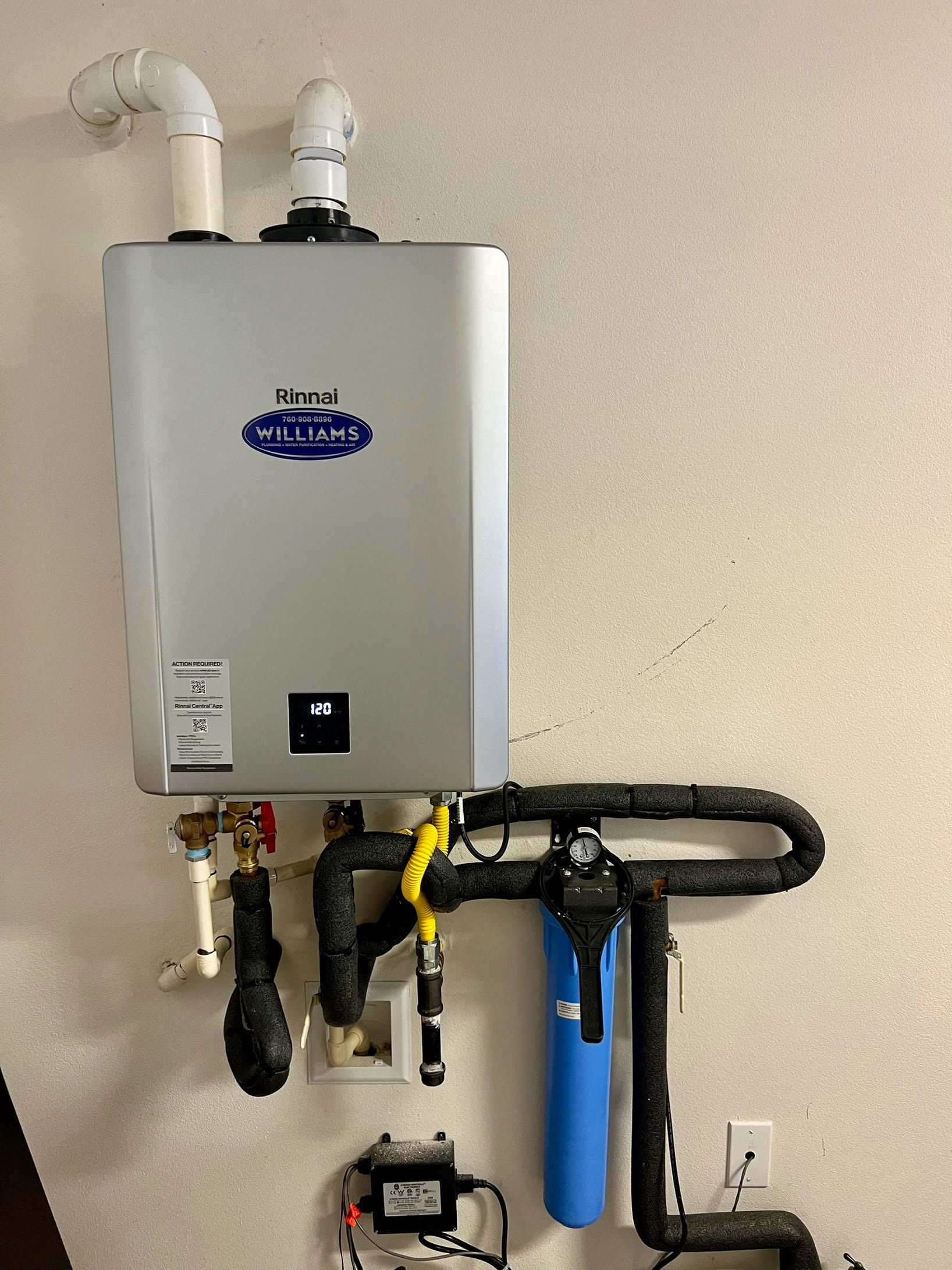 Tankless water heater mounted on a wall with pipes and a blue water filter.