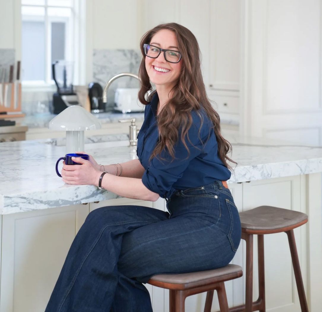 Woman smiling on a kitchen stool, holding a mug by a white marble island
