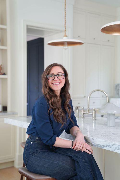 Woman seated on a kitchen island in a bright white kitchen, smiling at the camera