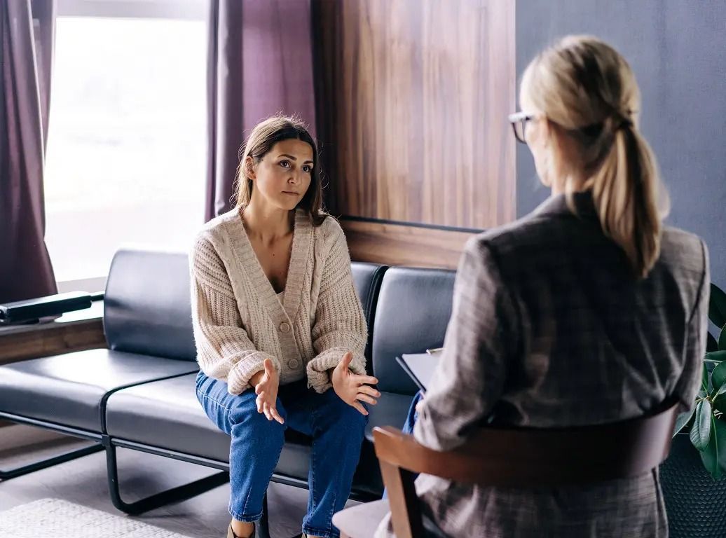 Two people in a counseling session, seated across from each other in a bright office.