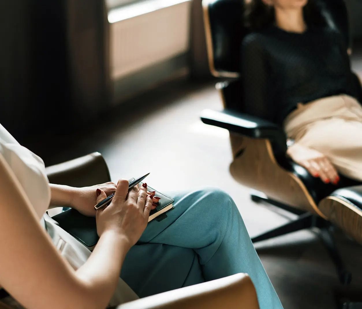 Two people seated in a counseling session, one holding a notebook in the foreground.