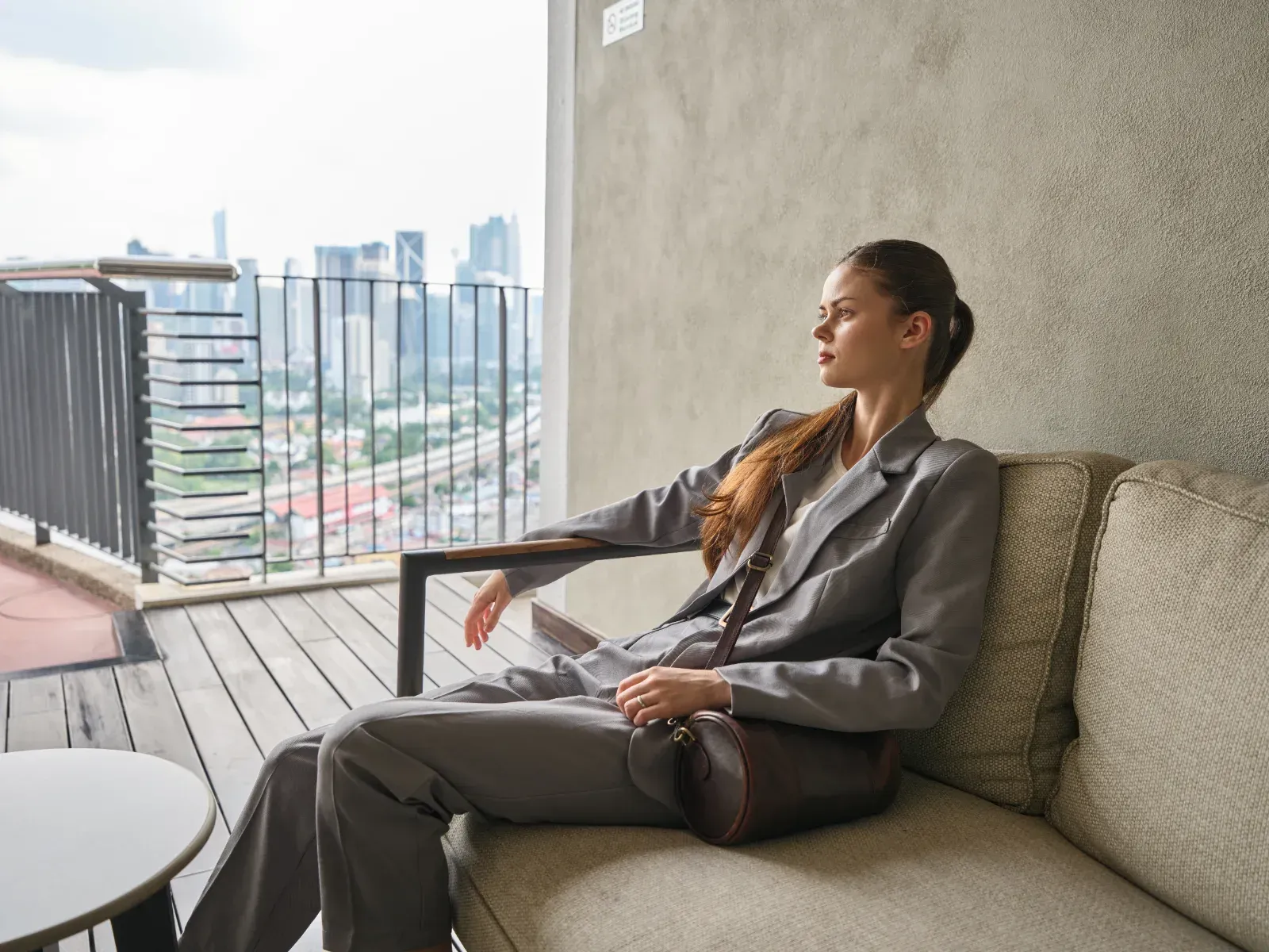 Person in a gray suit relaxing on a balcony sofa with a city skyline view