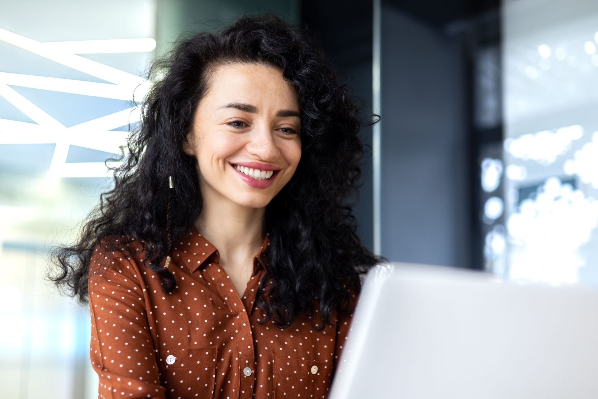 Smiling woman with curly hair using a laptop in a bright office setting