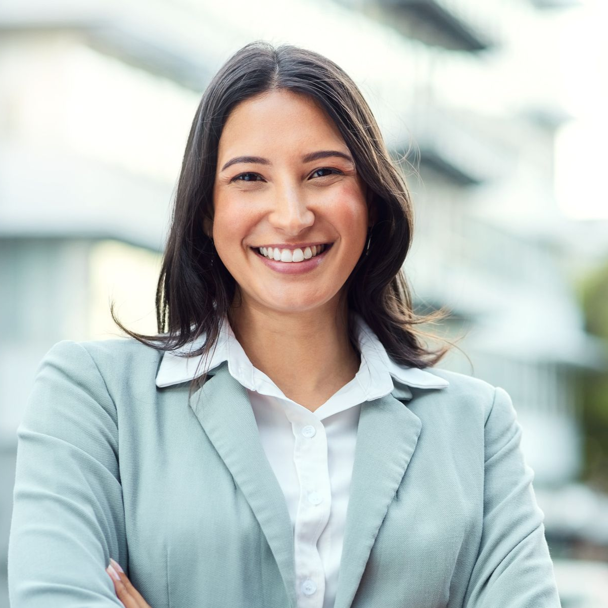 Smiling professional in a light blue blazer outdoors with a bright blurred background