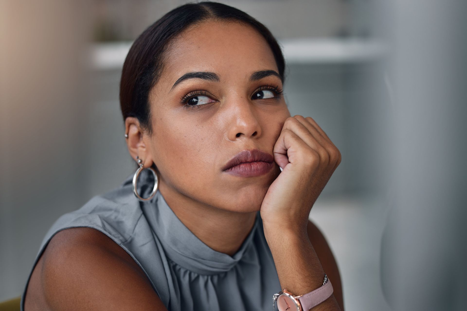 Woman resting her chin on her hand, looking off to the side in a gray sleeveless top indoors