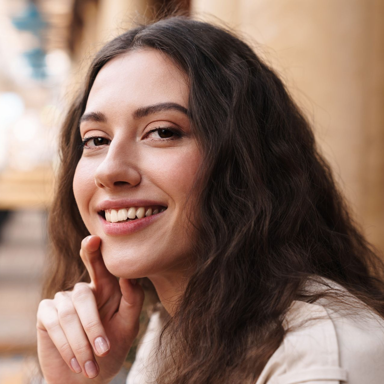 Smiling woman with wavy dark hair resting her chin on her hand outdoors