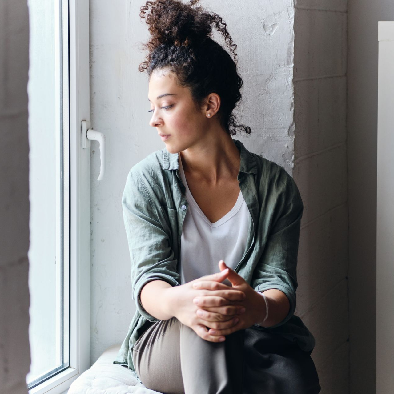 Woman sitting by a window, looking out thoughtfully in a softly lit room