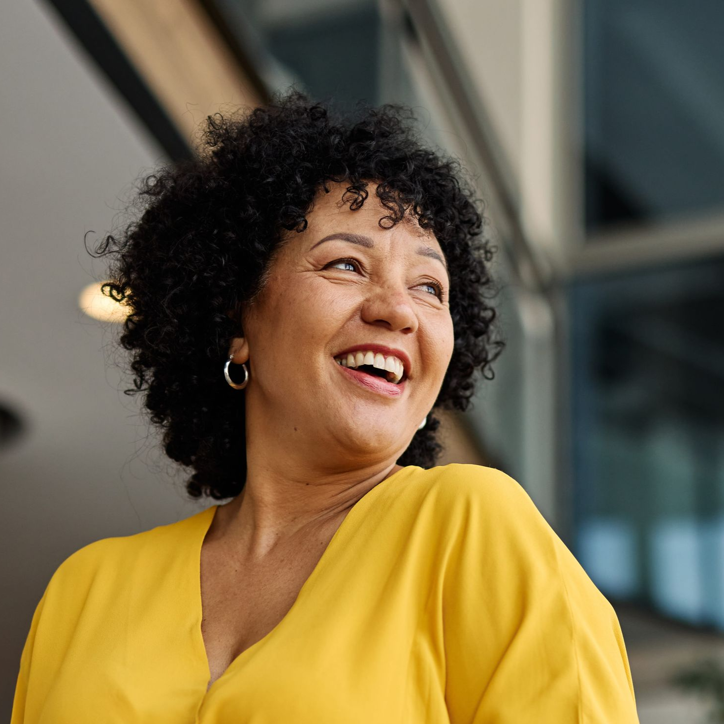 Smiling person in a yellow blouse looking off to the side in a modern indoor setting