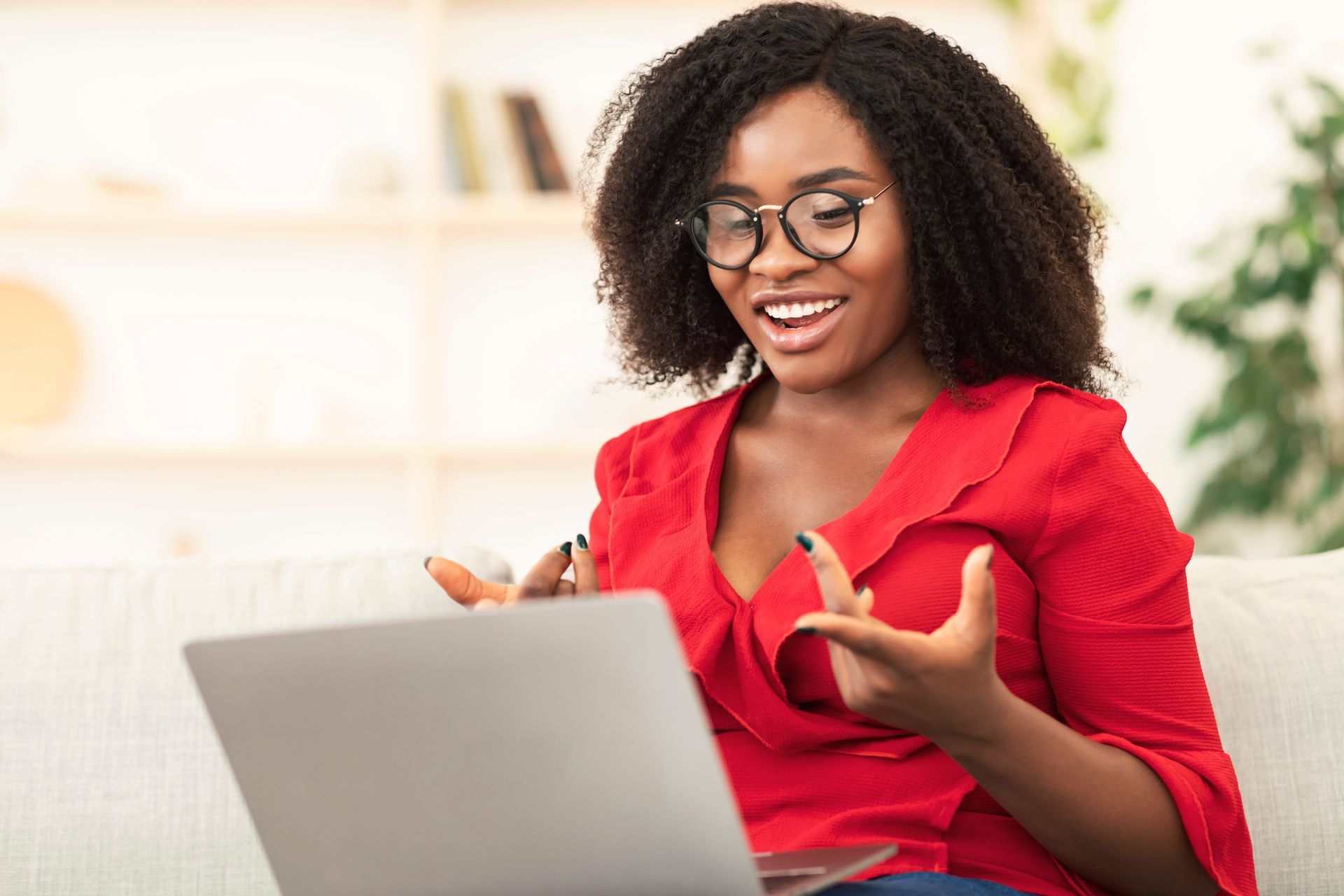 Smiling woman in a red blouse speaking on a video call from a laptop