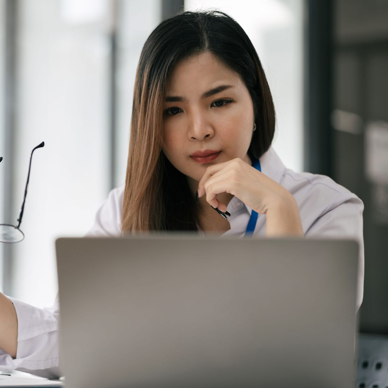 Woman at a desk looking thoughtfully over a laptop in a bright office