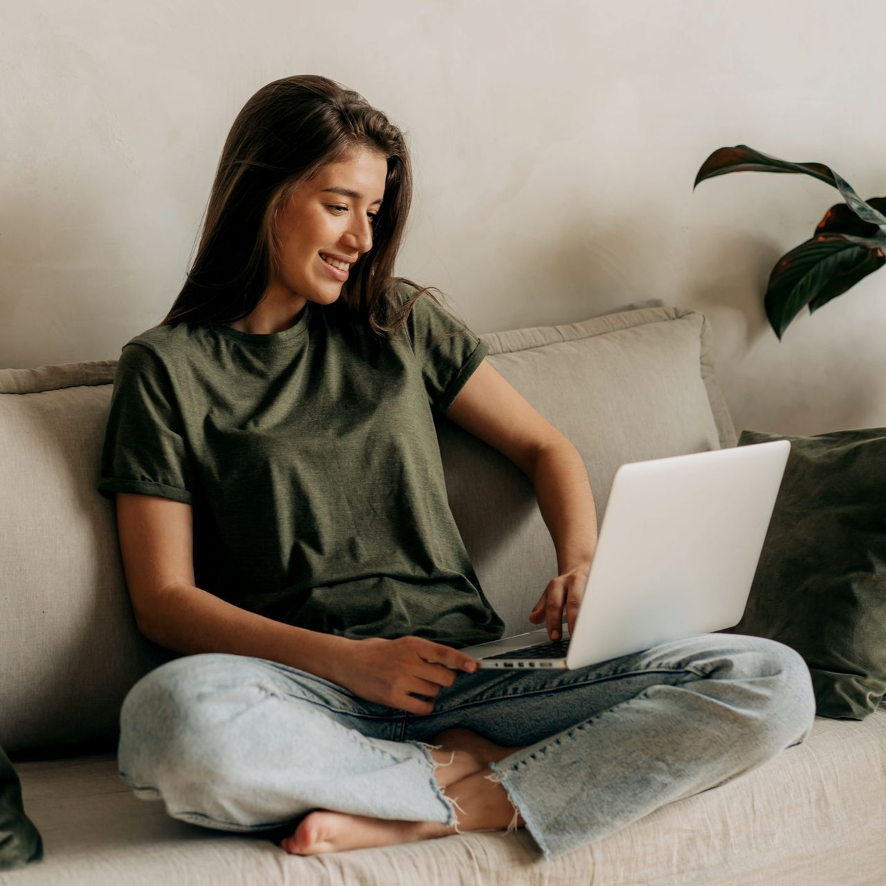 Woman sitting on a couch, smiling while using a laptop with a cat on her lap.