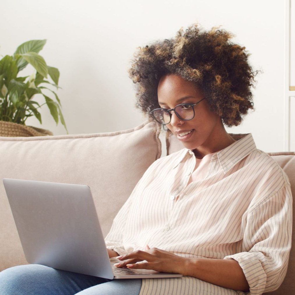 Person using a laptop on a couch in a bright living room