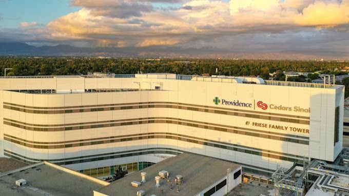 Aerial view of a large beige hospital building at sunset with Presidio and Cedars-Sinai logos.
