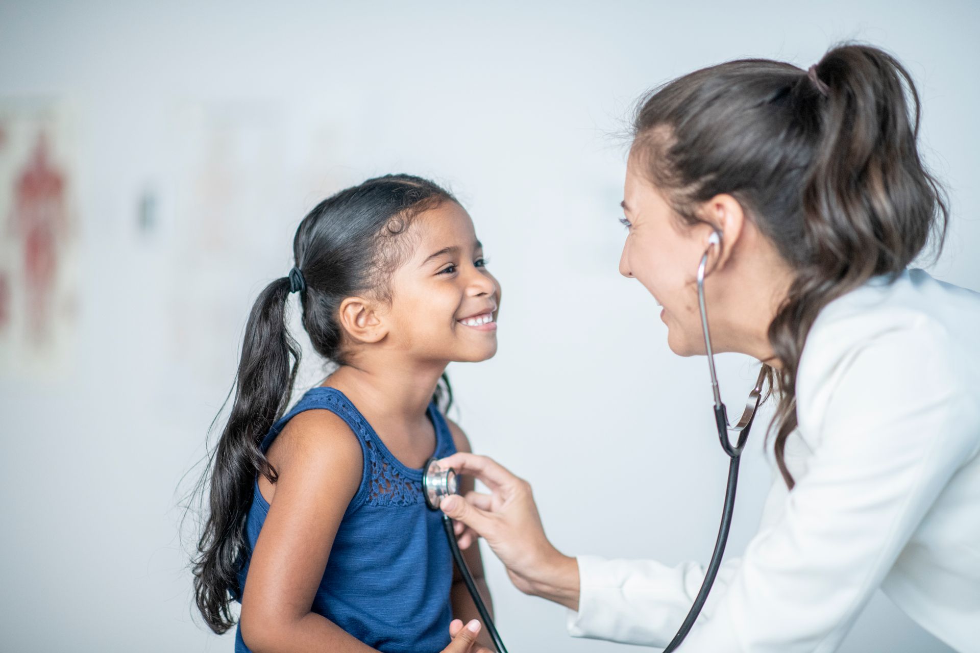 Doctor listening to child's heart with stethoscope; both smiling in a clinic setting.